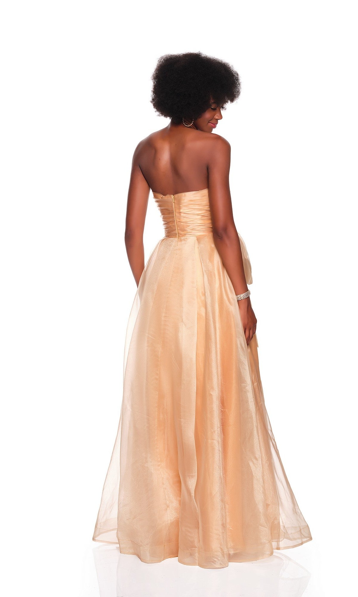 A woman stands with her back to the camera against a white background, wearing the Dave and Johnny 12629 long prom dress featuring a strapless ruched fitted bodice and tulle A-line skirt.
